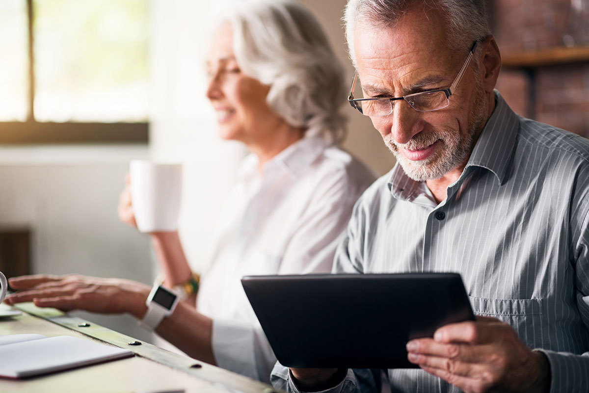 Two Senior People, the man looks closely at a tablet screen