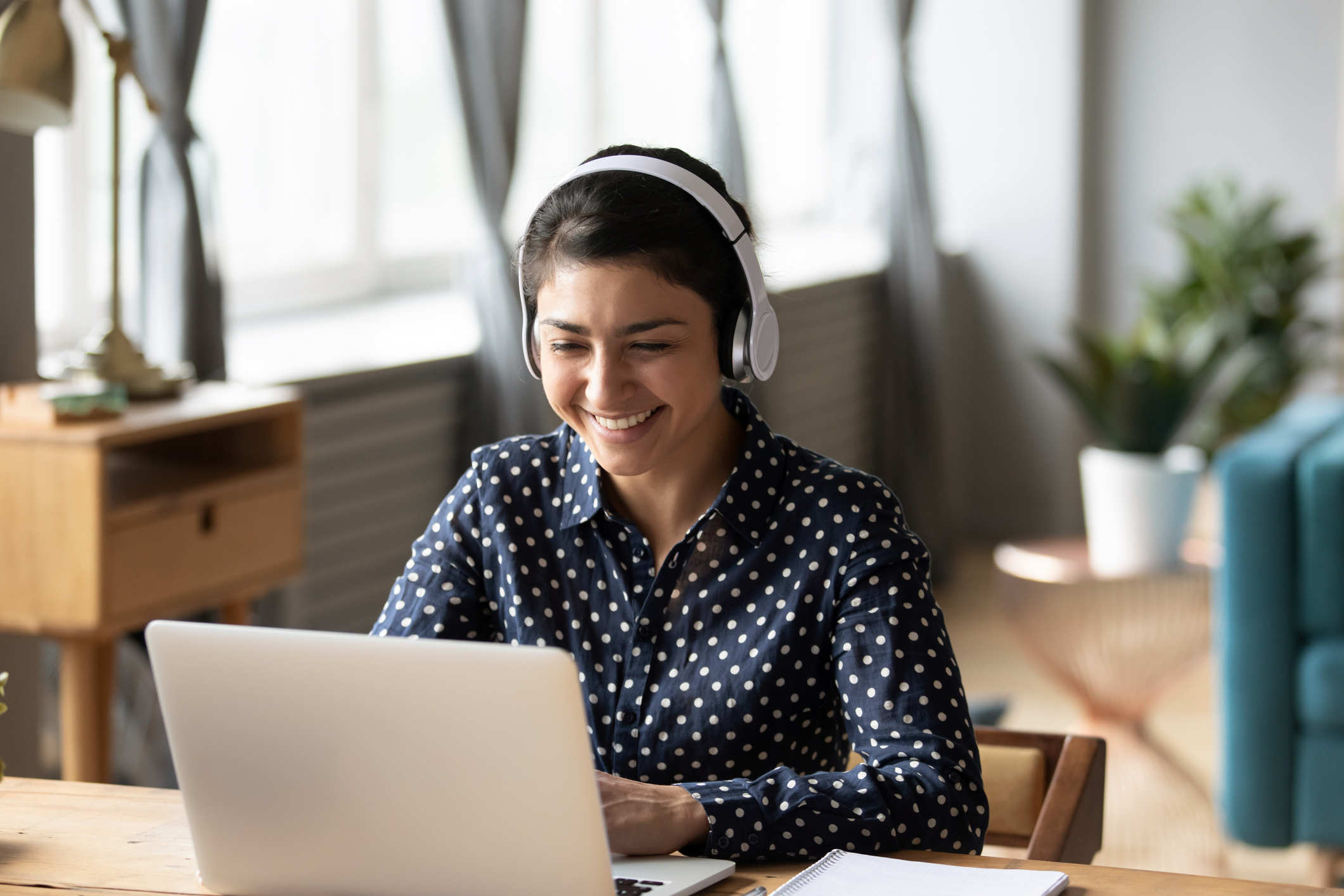 Image of a female person wearing headphones and smiling as she uses a laptop