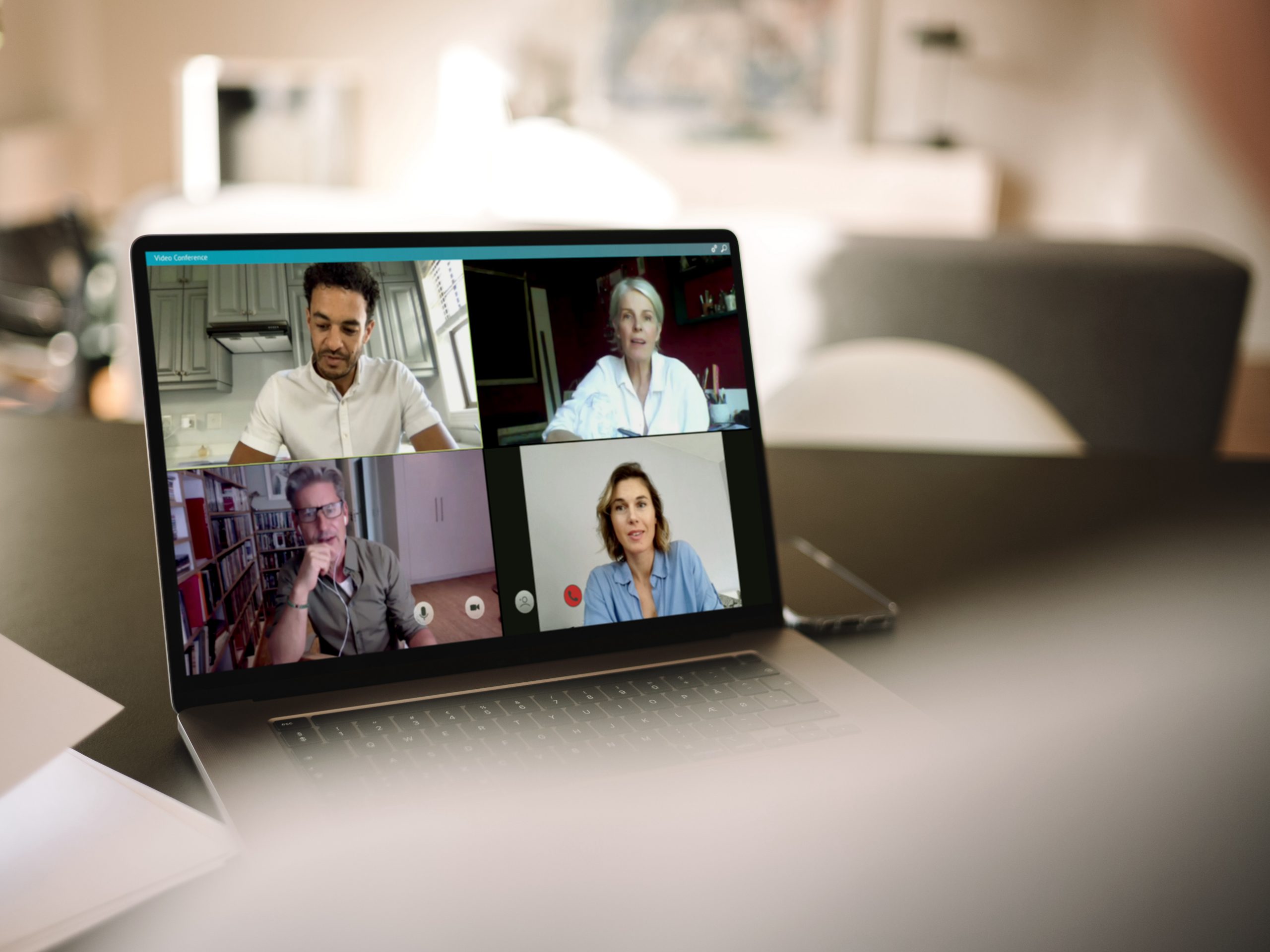 A laptop screen in a room showing an online video call. There are four people on the screen