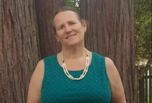 A woman standing in front of a tree wearing a green dress smiling.